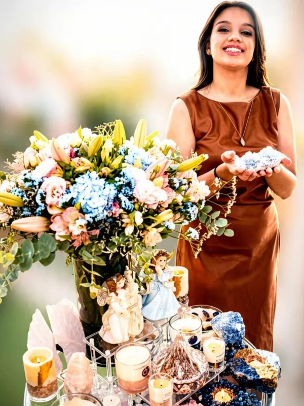 Marcelli com cristais nas mãos, atrás de uma mesa com flores, velas e pedras