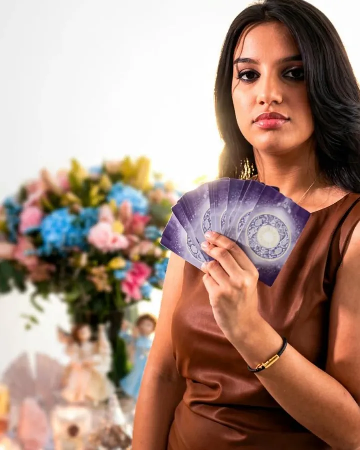 Marcelli segurando as cartas de tarô abertas em leque, diante de um arranjo de flores